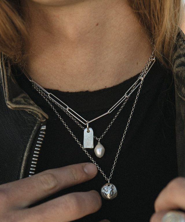 Person wearing multiple necklaces with pendants, focusing on the jewelry.