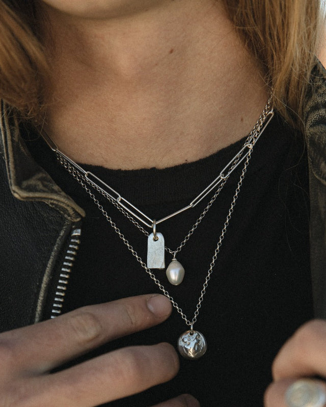 Person wearing multiple necklaces with pendants, focusing on the jewelry.