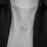 A silver necklace with a textured circular pendant worn by a person in a black zip-up jacket over a white t-shirt.