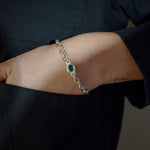 A close-up of a person's wrist wearing a silver chain bracelet with a central green oval stone, set against a dark navy shirt.