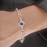 A sterling silver chain bracelet with a central diamond-shaped bezel holding a deep blue gemstone, shown worn on a person's wrist.