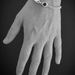 A silver chain bracelet with a central black oval stone, shown worn on a hand against a dark gray background.