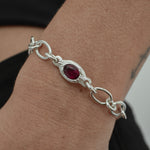 A sterling silver chain bracelet with a central oval red gemstone, shown worn on a person's wrist.