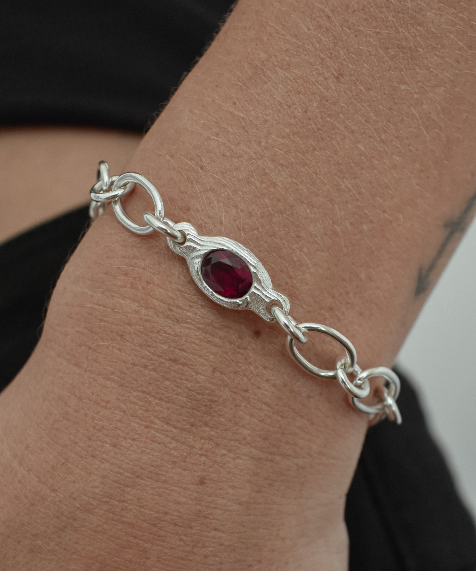 A sterling silver chain bracelet with a central oval red gemstone, shown worn on a person's wrist.