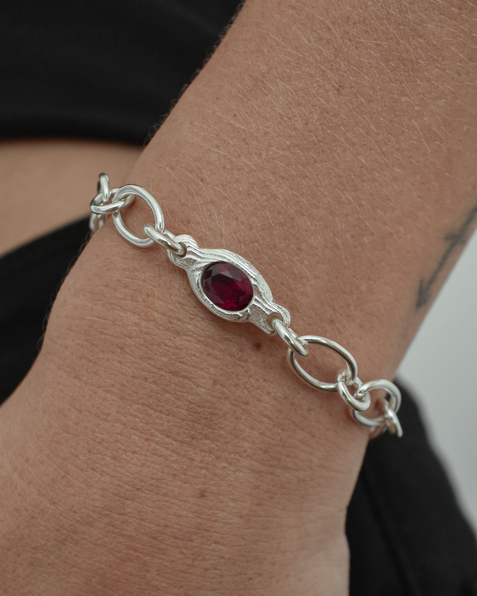 A sterling silver chain bracelet with a central oval red gemstone, shown worn on a person's wrist.