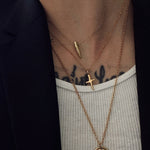 Close-up of layered gold necklaces with a cross pendant on a person wearing a black jacket and white shirt.