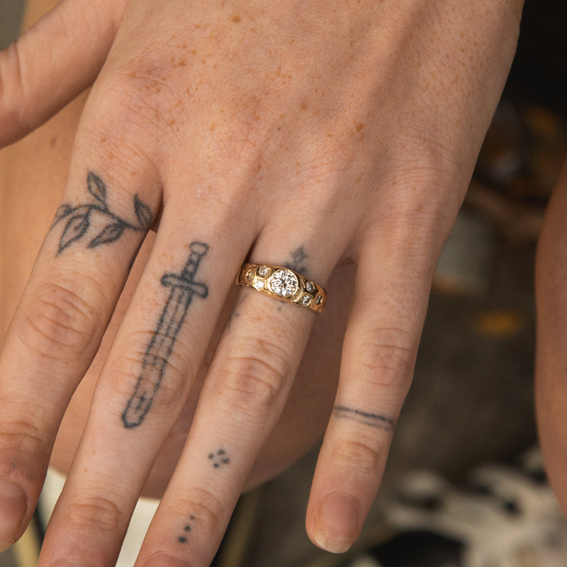 Close-up of a hand with tattoos and a gold ring on a blurred natural background