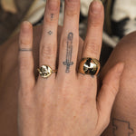 Close-up of a hand wearing two gold rings with tattoos on the fingers.