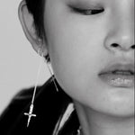 Close-up of a person wearing a dangling earring with a cross design.