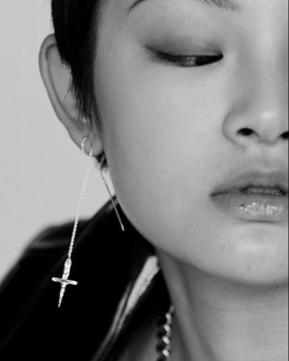 Close-up of a person wearing a dangling earring with a cross design.