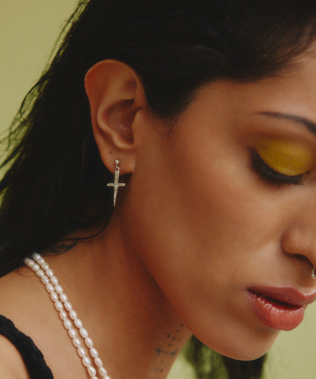 Close-up of a woman wearing a cross earring with a blurred background