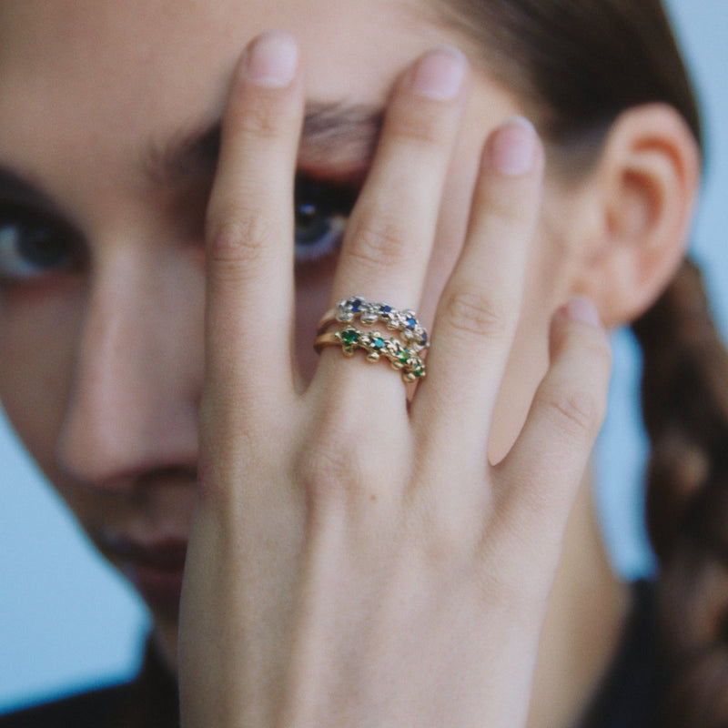 Close-up of a hand with a ring featuring green gemstones, held near the face.