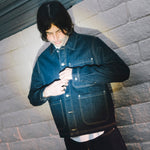 Person wearing a denim jacket against a textured wall.