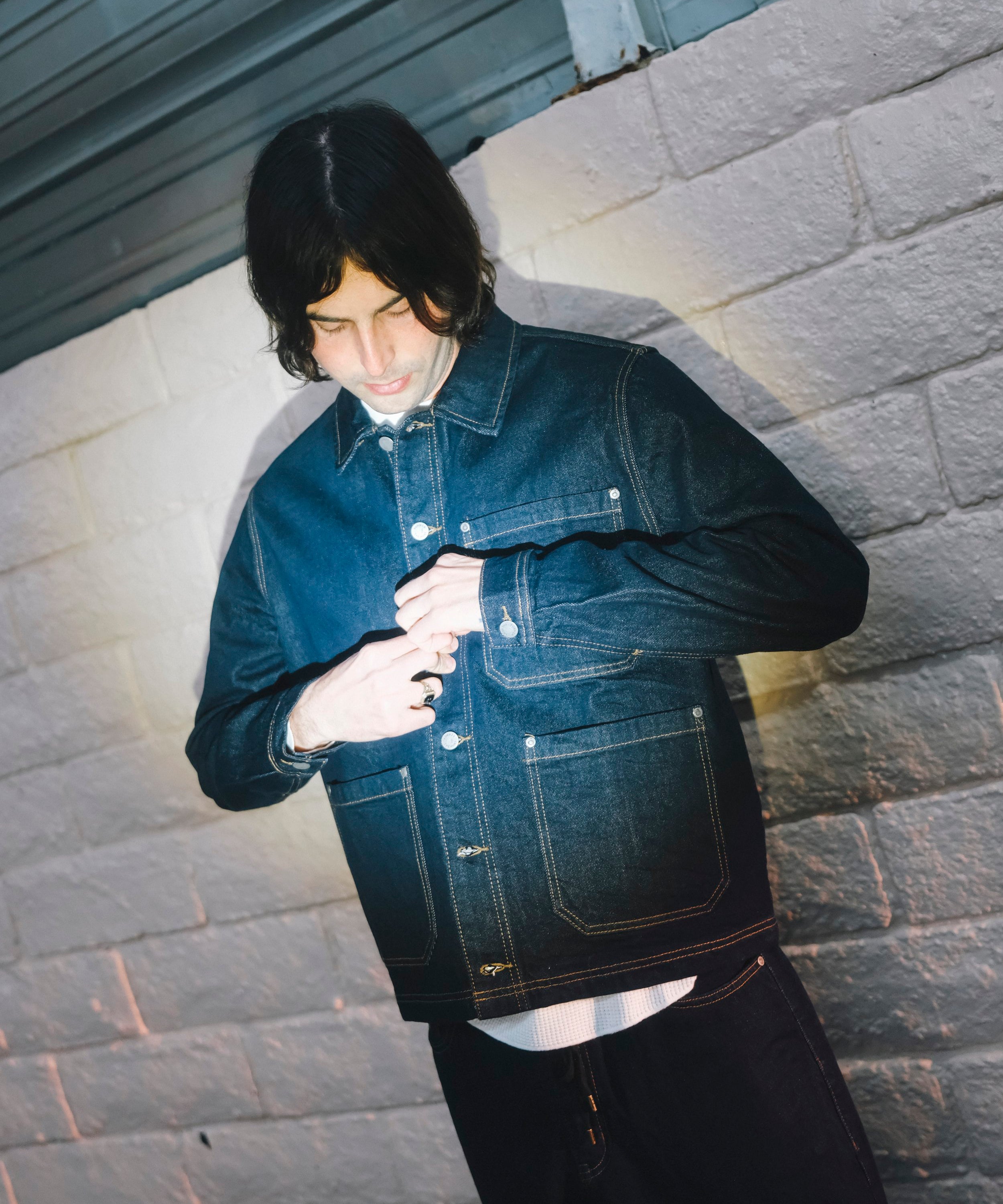 Person wearing a denim jacket against a textured wall.