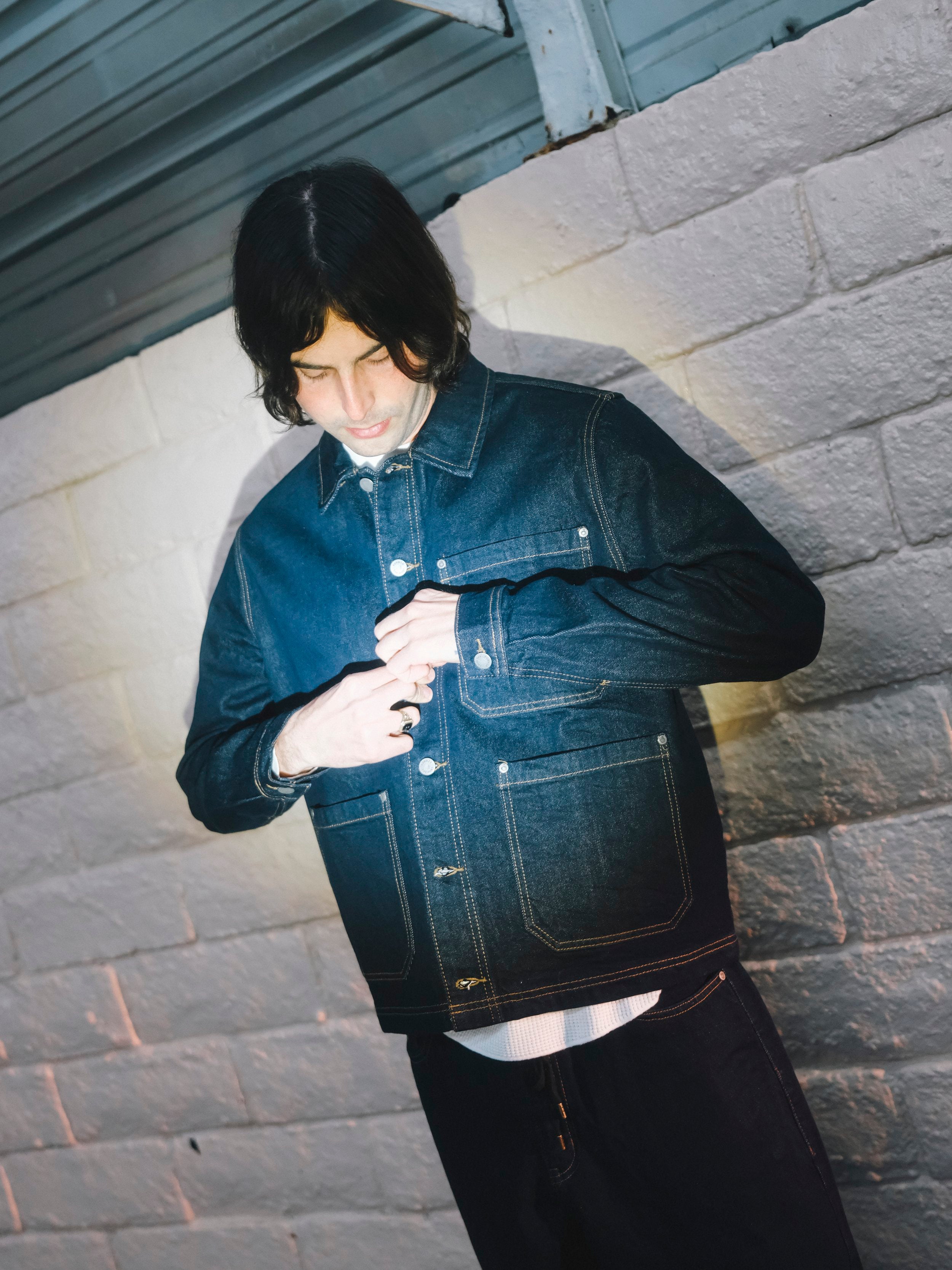 Person wearing a denim jacket against a textured wall.