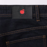 Close-up of dark denim jeans with a brand label featuring a red apple logo on a light gray background.