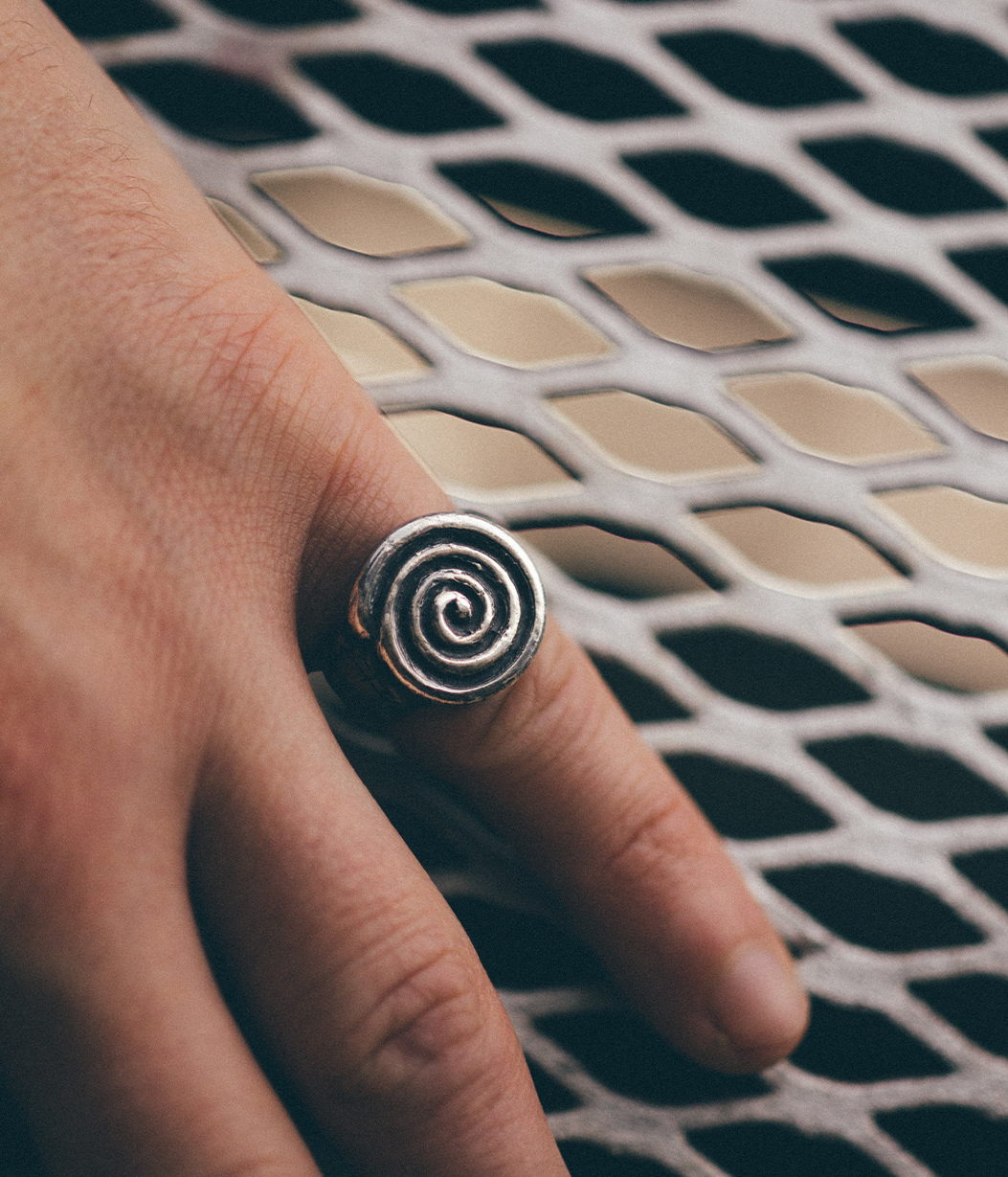 A close-up of a hand wearing a silver spiral ring, resting on a white metal mesh surface.