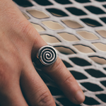 A close-up of a hand wearing a silver spiral ring, resting on a white metal mesh surface.