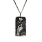 A rectangular silver pendant necklace featuring an embossed hand holding a tulip, suspended from a silver curb chain against a plain white background.