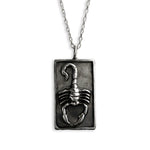 A silver-toned rectangular pendant necklace featuring a raised scorpion design, suspended from a matching chain against a plain white background.