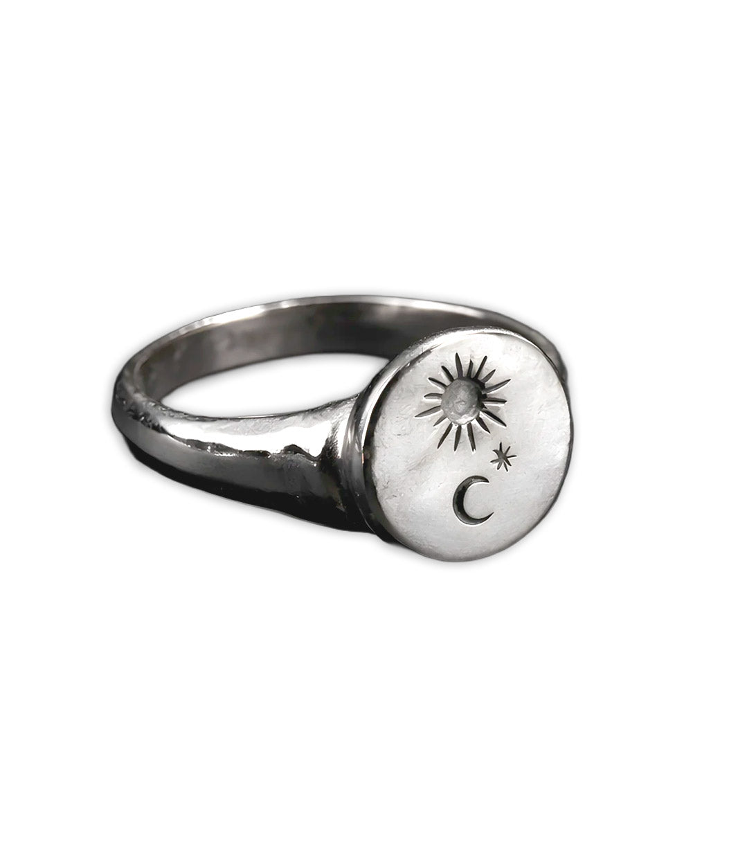 A silver signet ring with a circular face engraved with a sunburst, a crescent moon, and a small star, shown on a plain white background.