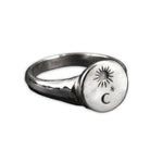 A silver signet ring with a circular face engraved with a sunburst, a crescent moon, and a small star, shown on a plain white background.