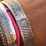 Close-up of a wrist wearing multiple metallic bracelets on a wooden surface