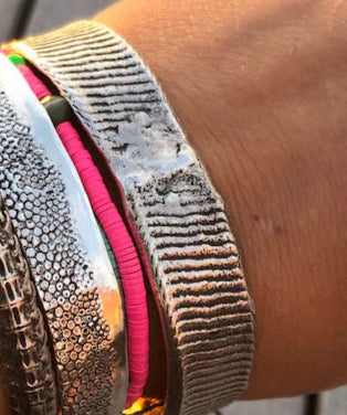 Close-up of a wrist wearing multiple metallic bracelets on a wooden surface