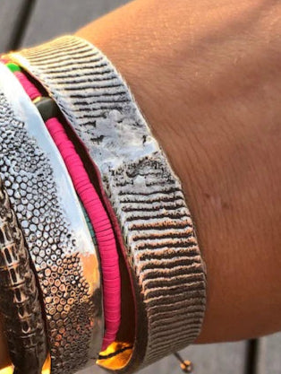 Close-up of a wrist wearing multiple metallic bracelets on a wooden surface