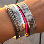 Close-up of a wrist wearing multiple metallic bracelets on a wooden surface