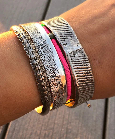 Close-up of a wrist wearing multiple metallic bracelets on a wooden surface