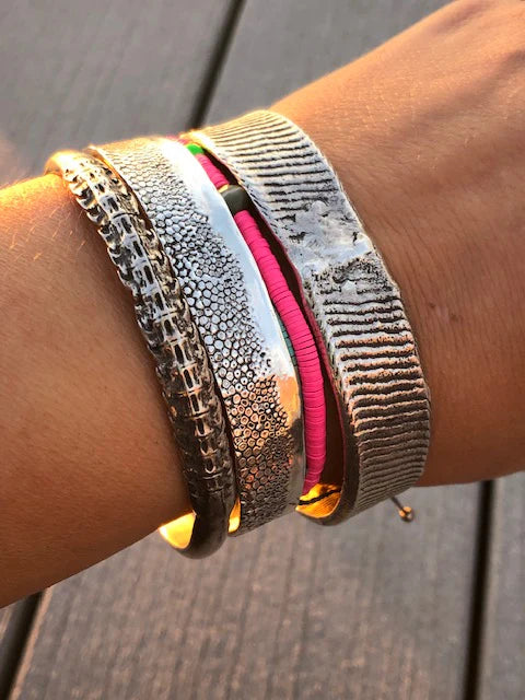 Close-up of a wrist wearing multiple metallic bracelets on a wooden surface