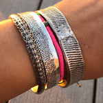 Close-up of a wrist wearing multiple metallic bracelets on a wooden surface