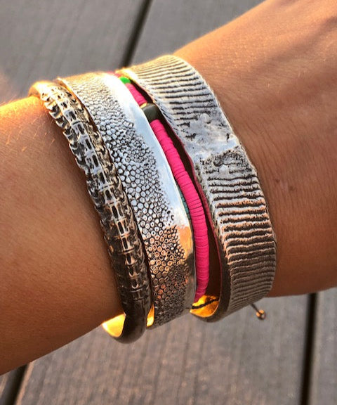 Close-up of a wrist wearing multiple metallic bracelets on a wooden surface