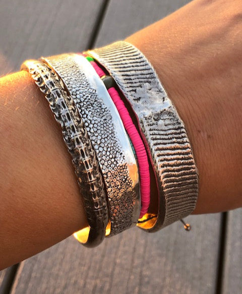 Close-up of a wrist wearing multiple metallic bracelets on a wooden surface