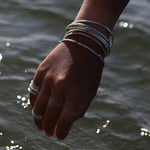 Hand with bracelets reaching towards water with sunlight reflecting off the surface