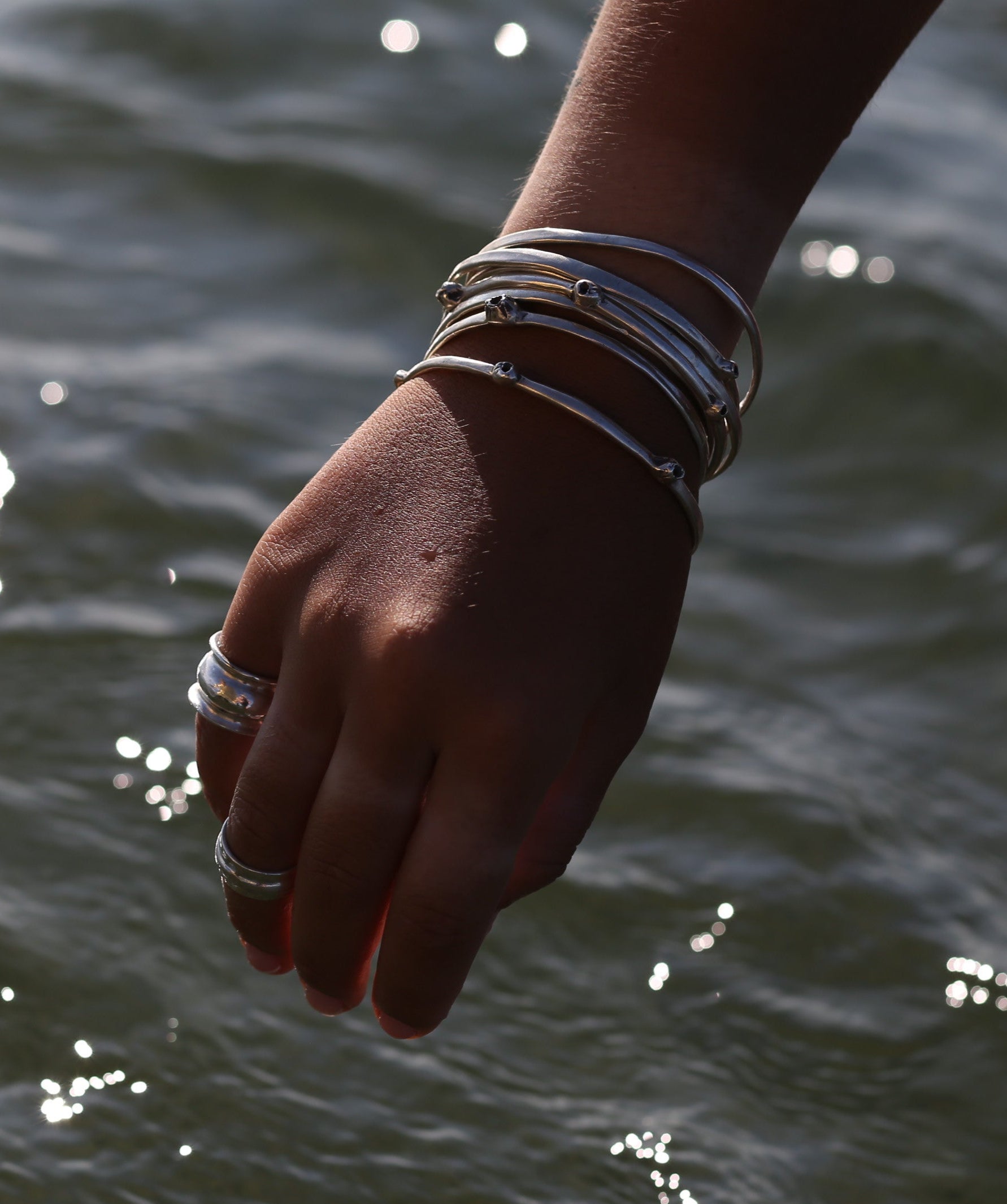 Hand with bracelets reaching towards water with sunlight reflecting off the surface