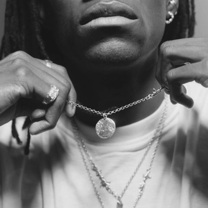 Person wearing layered necklaces with a close-up of the neck and hands.