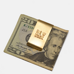 Gold 'New York' money clip on a $20 bill with a white background