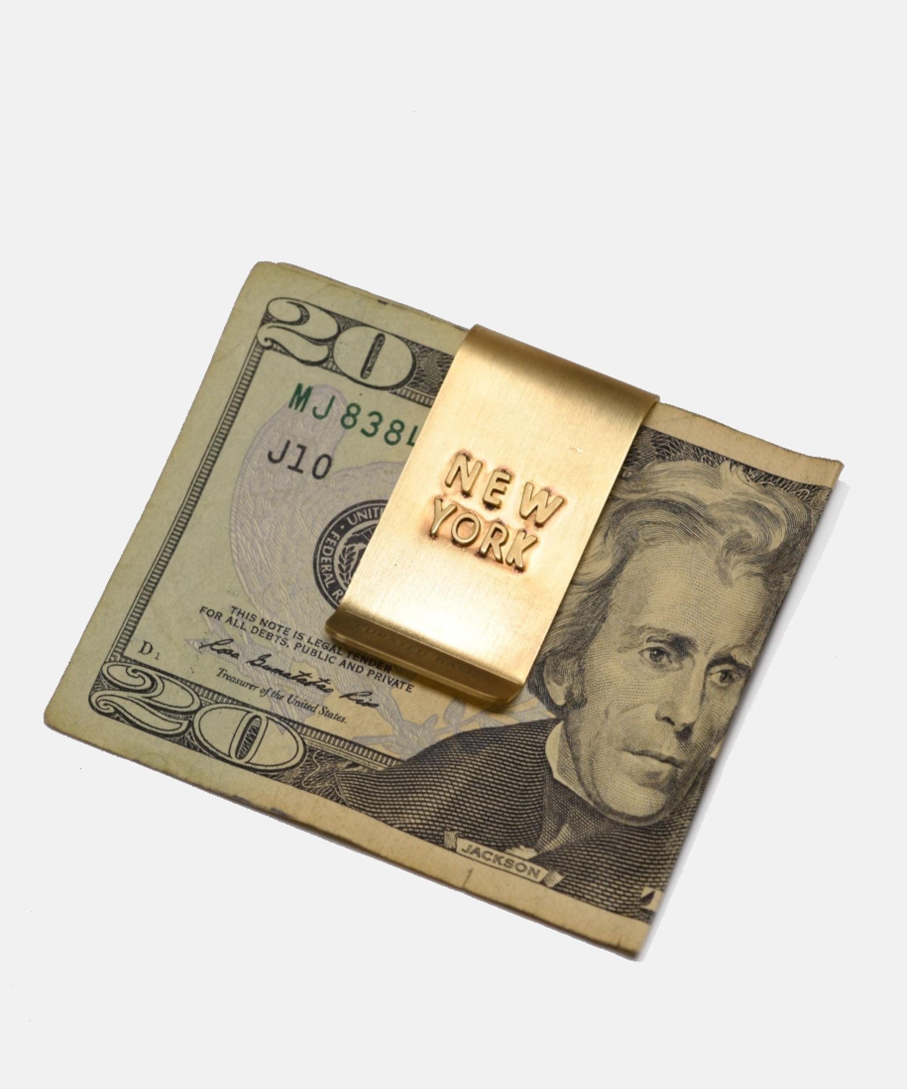 Gold 'New York' money clip on a $20 bill with a white background