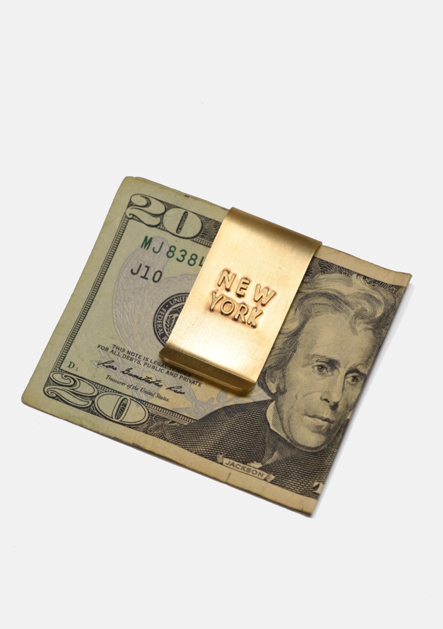 Gold 'New York' money clip on a $20 bill with a white background
