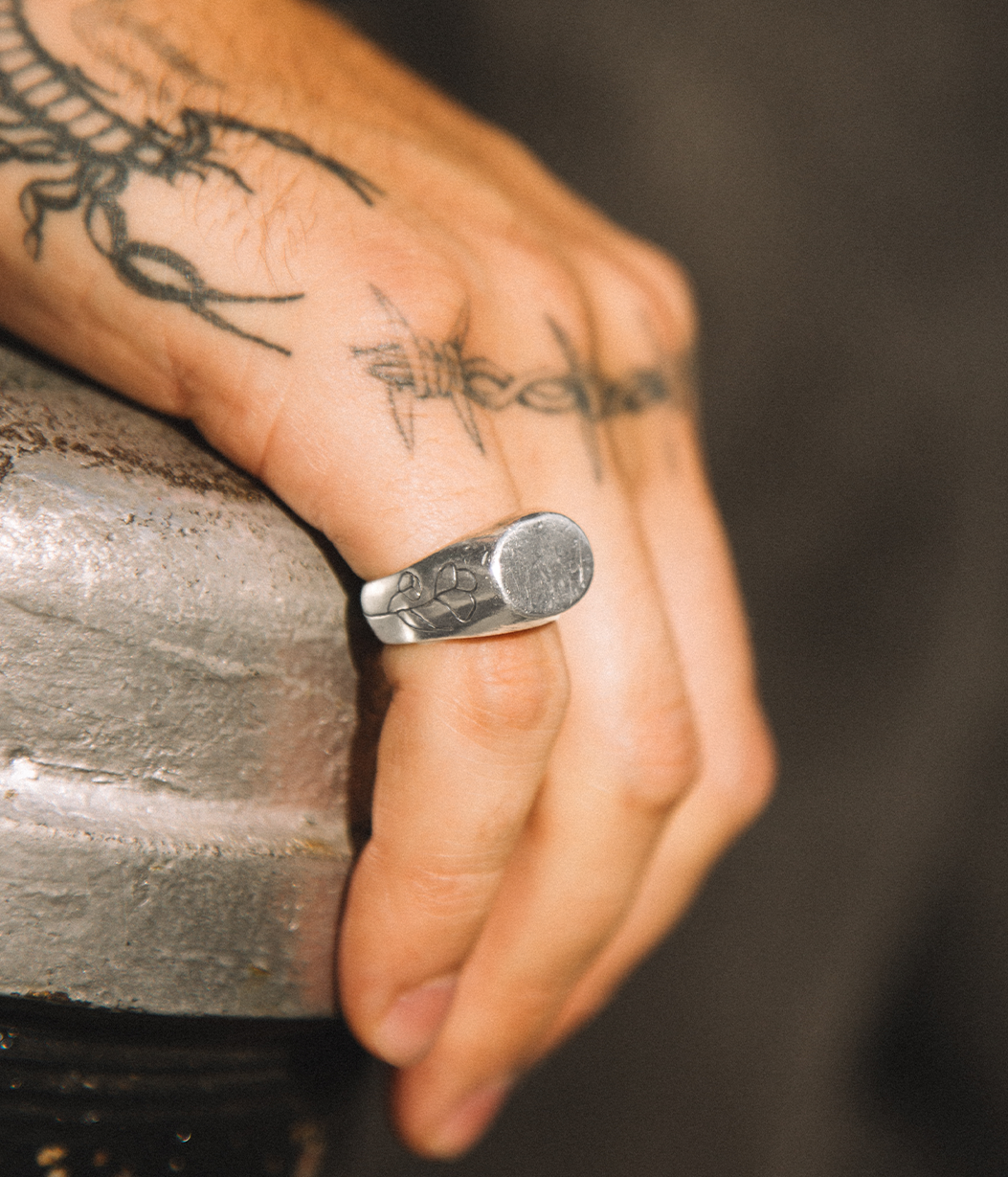 Hand wearing a silver ring with a textured design, against a blurred background.