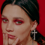 Close-up of a person with red makeup and earrings against a red background