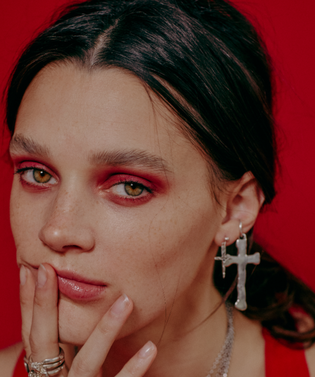 Close-up of a person with red makeup and earrings against a red background