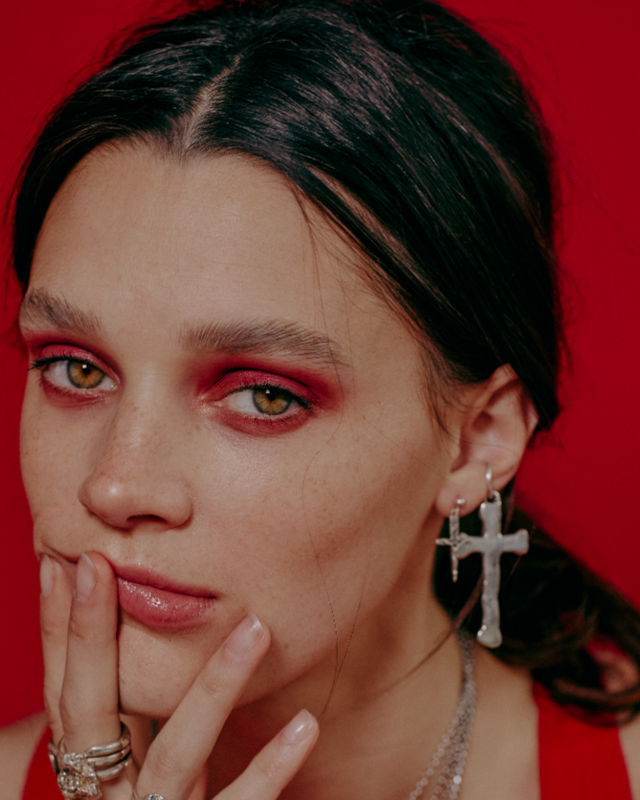 Close-up of a person with red makeup and earrings against a red background