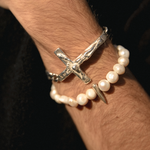 Silver cross bracelet and pearl bracelet on a wrist against a dark background