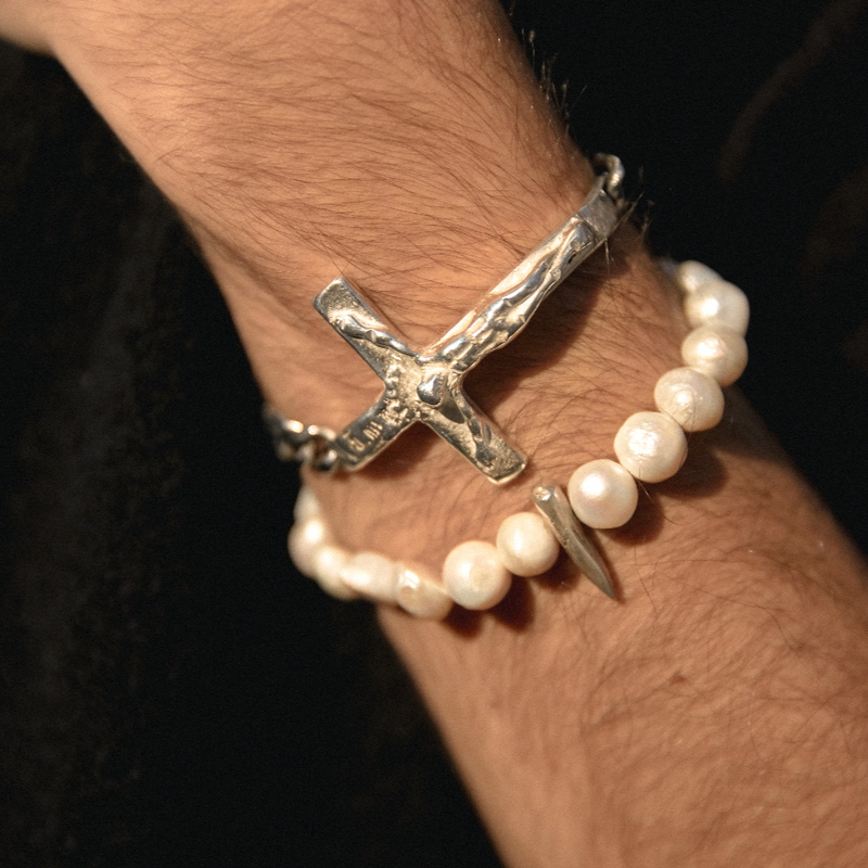 Silver cross bracelet and pearl bracelet on a wrist against a dark background