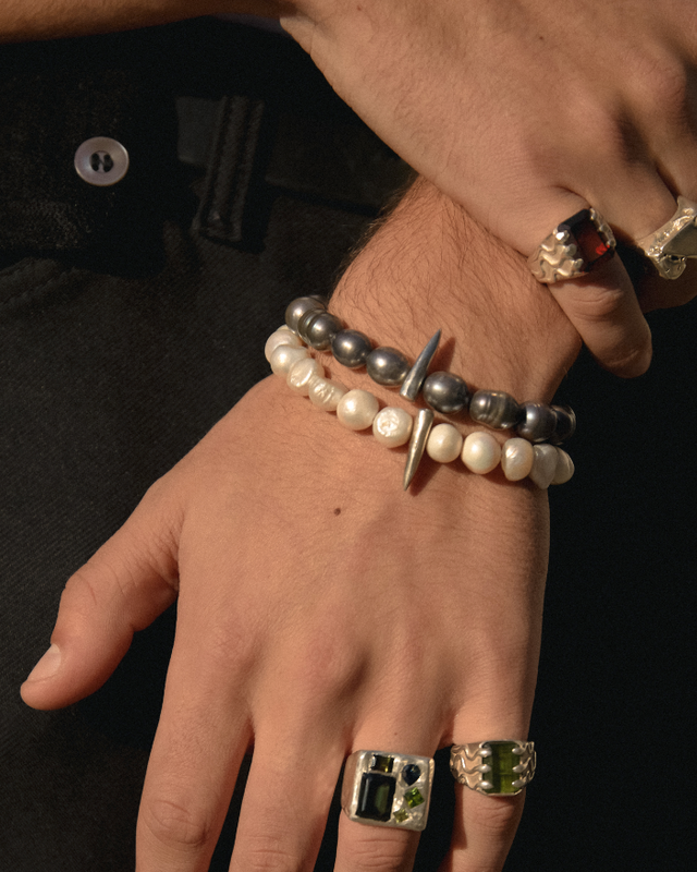 Close-up of a hand wearing multiple rings and bracelets on a dark background