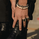 Close-up of a person's hand wearing a bracelet and ring, holding a black boot.
