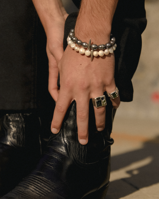 Close-up of a person's hand wearing a bracelet and ring, holding a black boot.